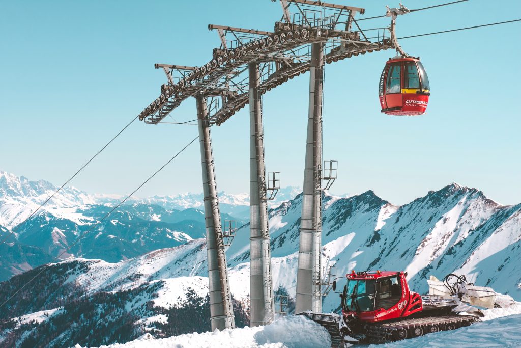 un chasse neige rouge qui passe sous un téléphérique rouge à la montagne en hiver