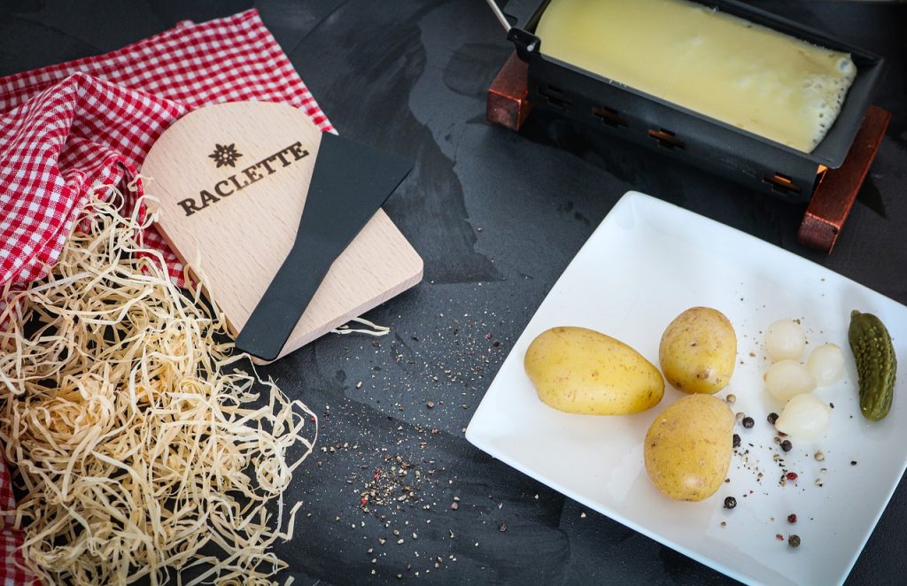 raclette avec assiette de pommes de terre et poêlon de fromage fondu