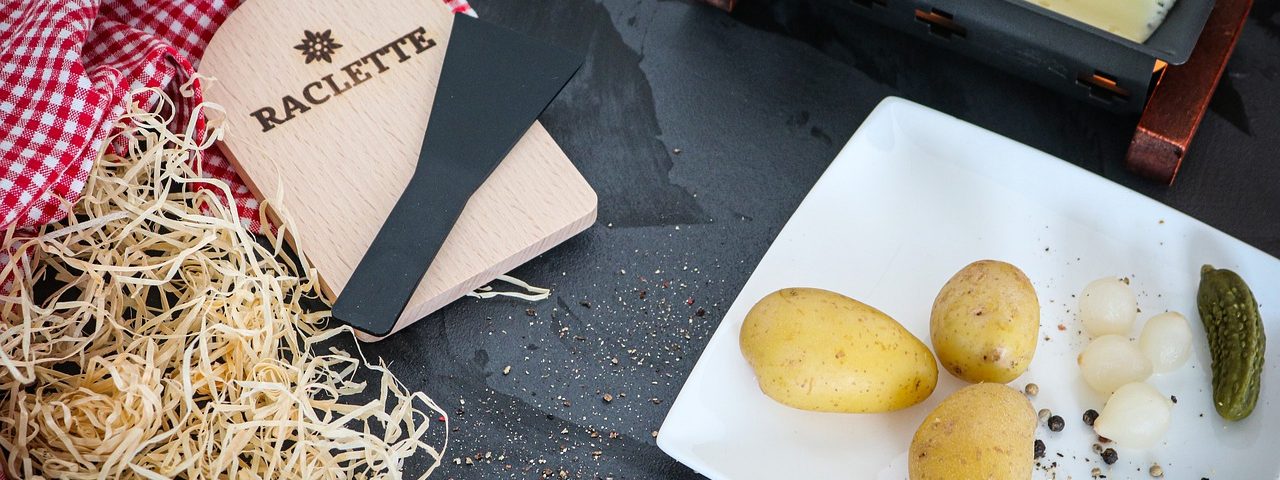 raclette avec assiette de pommes de terre et poêlon de fromage fondu